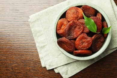 Tasty apricots in bowl on wooden table, top view and space for text. Dried fruits
