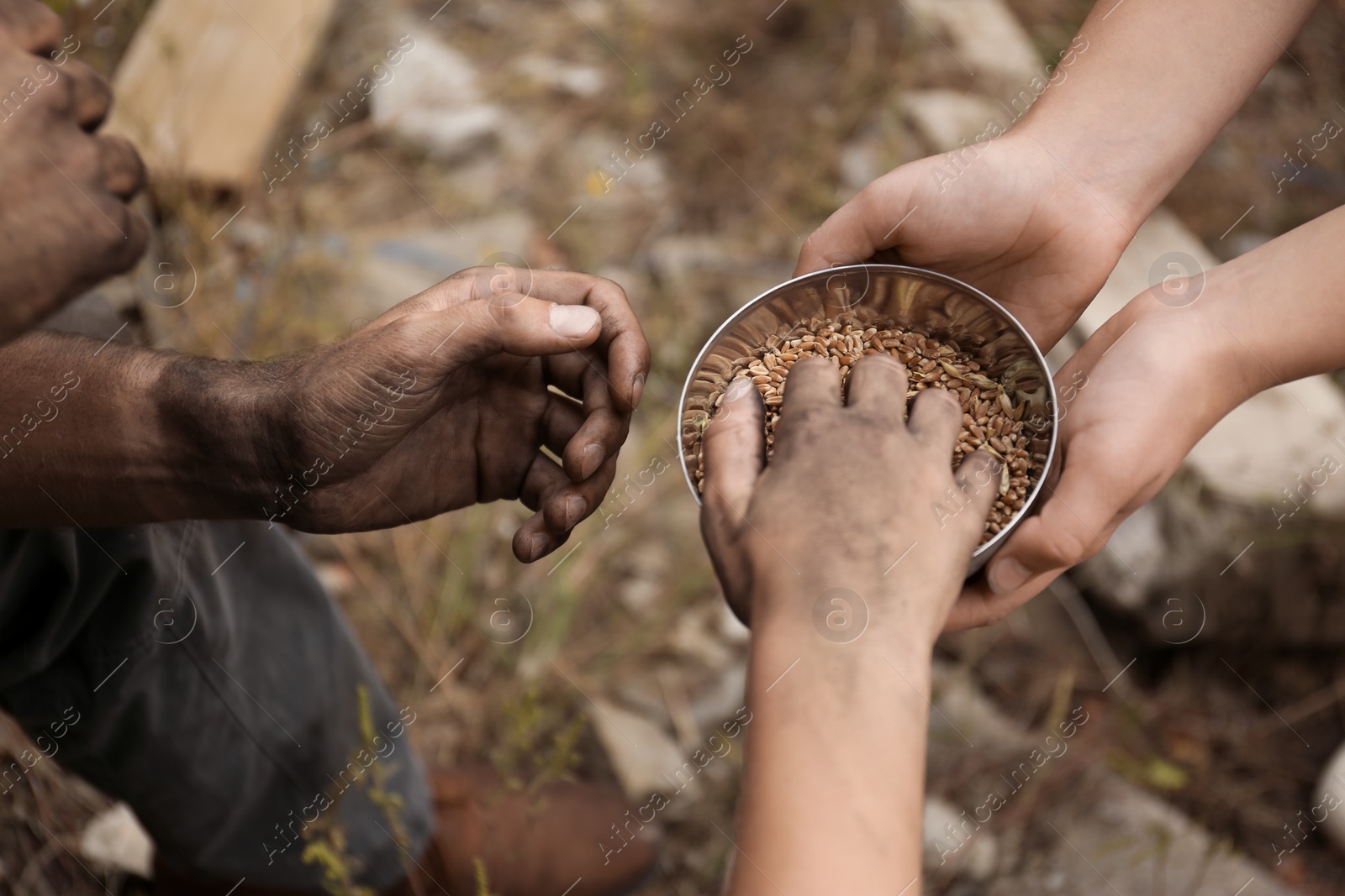 Photo of Woman giving poor homeless people bowl of wheat outdoors, closeup