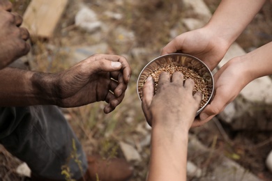 Woman giving poor homeless people bowl of wheat outdoors, closeup