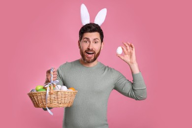 Portrait of happy man in cute bunny ears headband holding Easter eggs on pink background