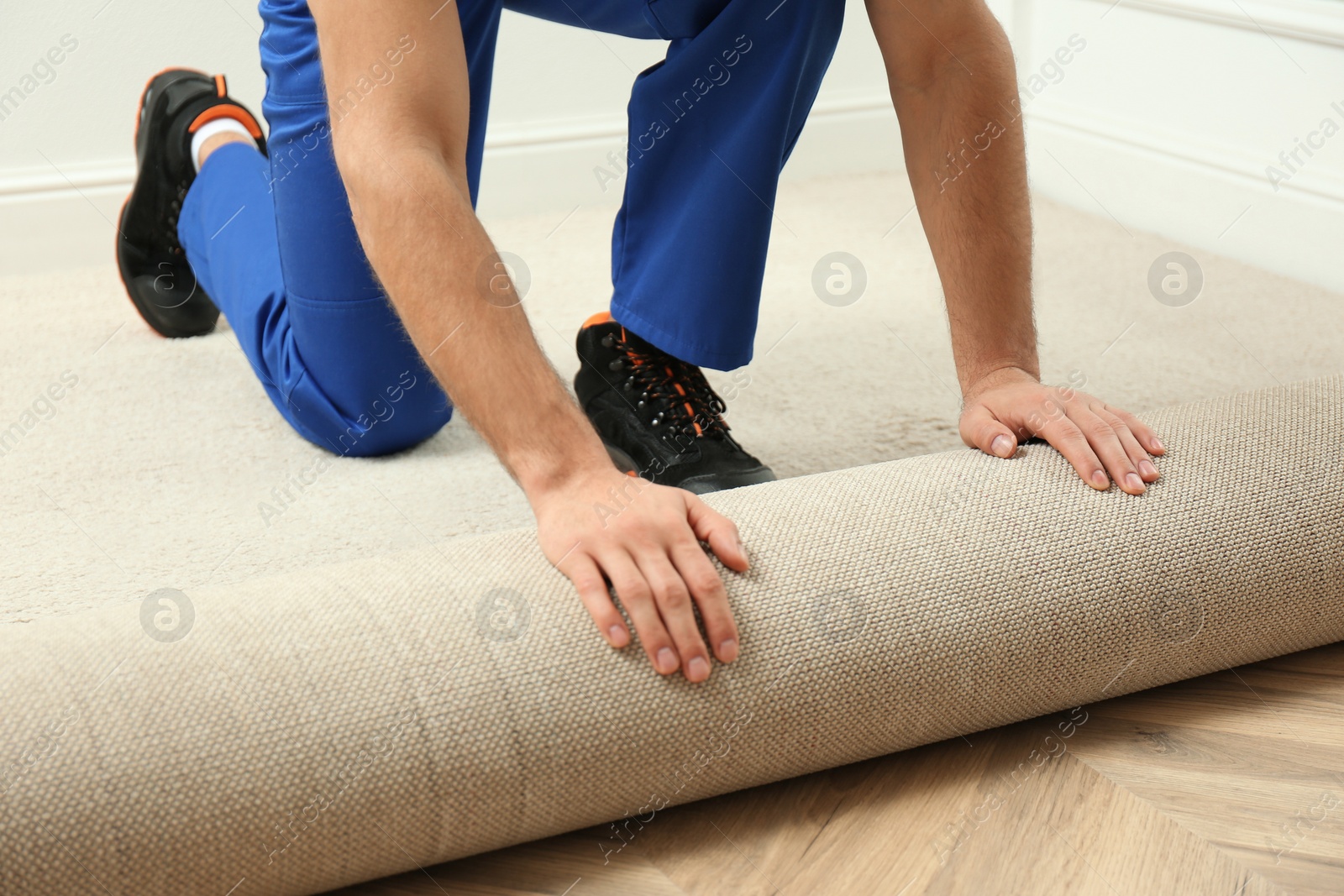 Photo of Worker rolling out new carpet flooring indoors, closeup