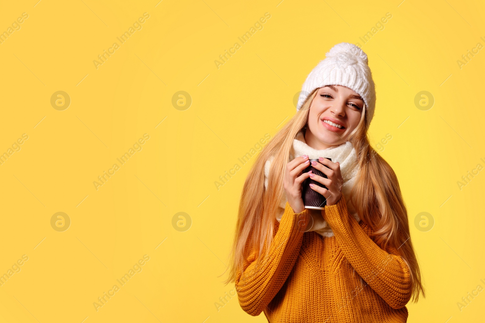 Photo of Portrait of young woman in stylish hat and sweater with paper coffee cup on color background, space for text. Winter atmosphere