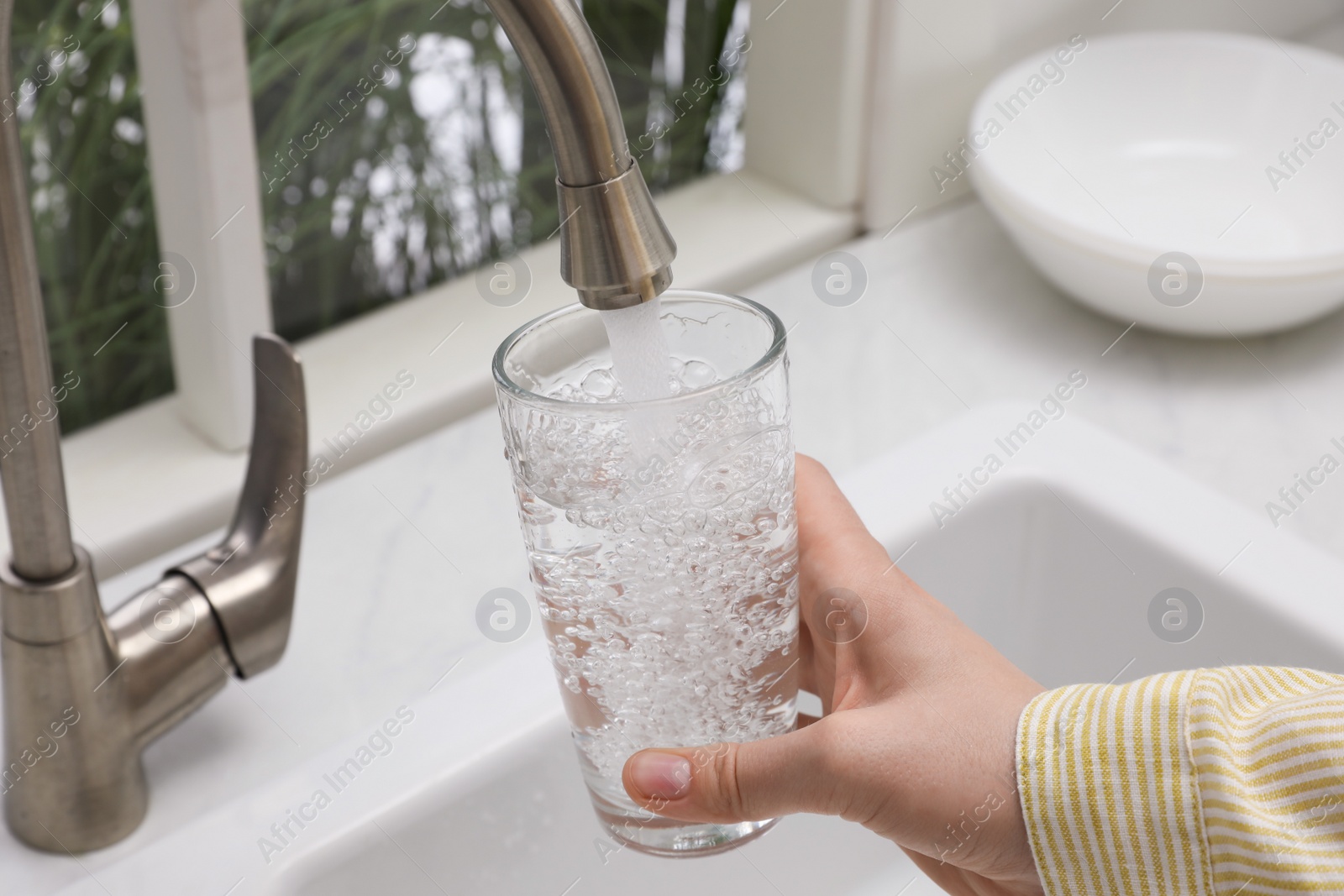 Photo of Woman filling glass with water from tap in kitchen, closeup