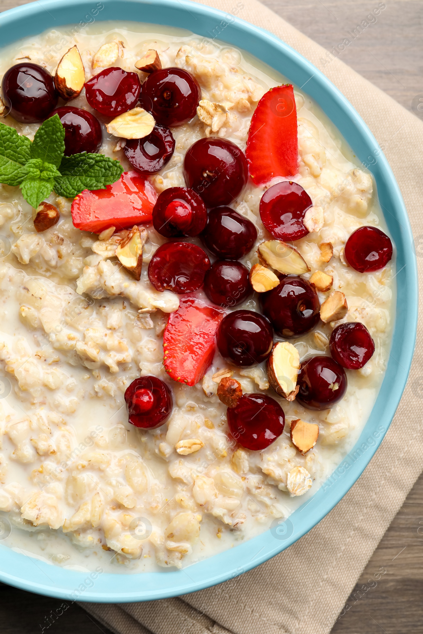 Photo of Bowl of oatmeal porridge served with berries on wooden table, top view