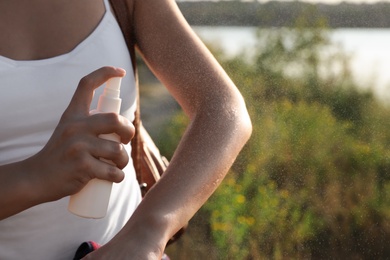 Photo of Woman applying insect repellent onto arm outdoors, closeup. Space for text