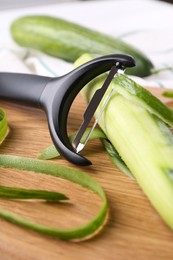 Photo of Fresh cucumber, peels and peeler on wooden board, closeup