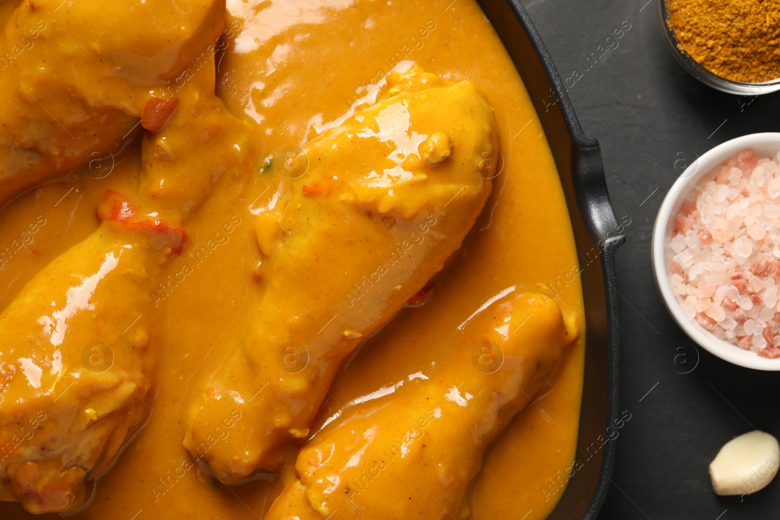 Photo of Tasty chicken curry and ingredients on black textured table, flat lay