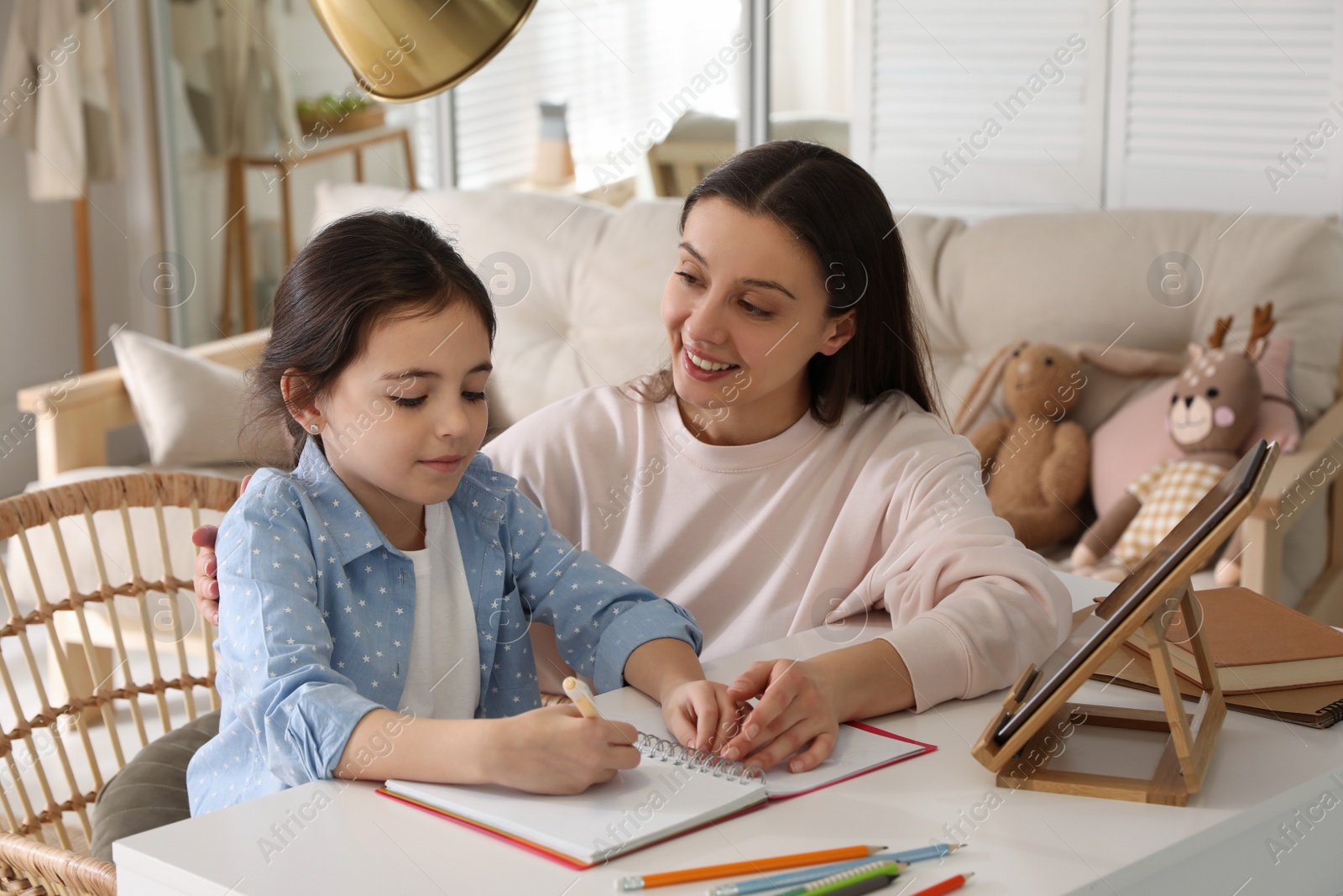 Photo of Mother helping her daughter with homework using tablet at home