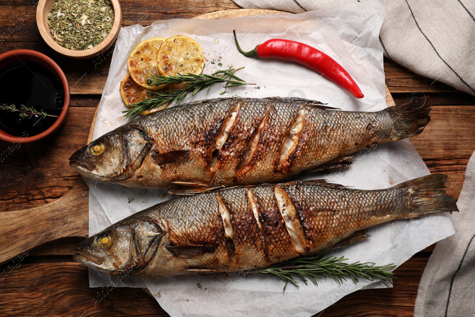 Photo of Delicious baked sea bass fish and ingredients on wooden table, flat lay