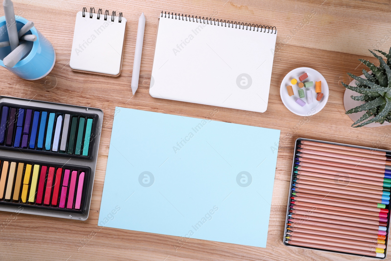 Photo of Layout with blank papers, soft pastels and other drawing supplies on wooden table at artist's workplace, top view. Space for design