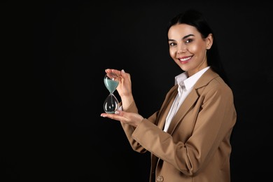Photo of Businesswoman holding hourglass on black background, space for text. Time management