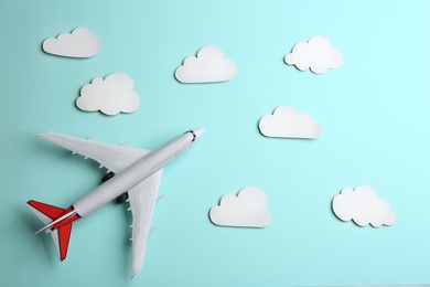 Toy airplane and clouds on light blue background, flat lay