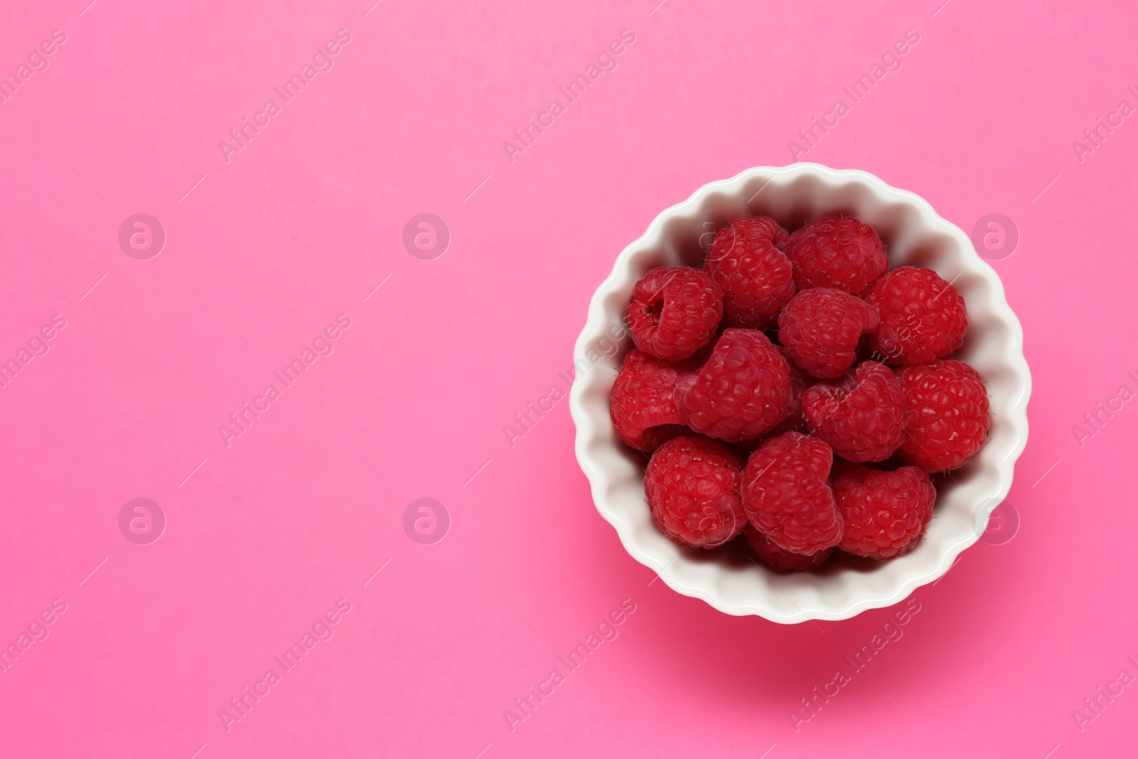 Photo of Bowl of fresh delicious raspberries on pink background, top view. Space for text