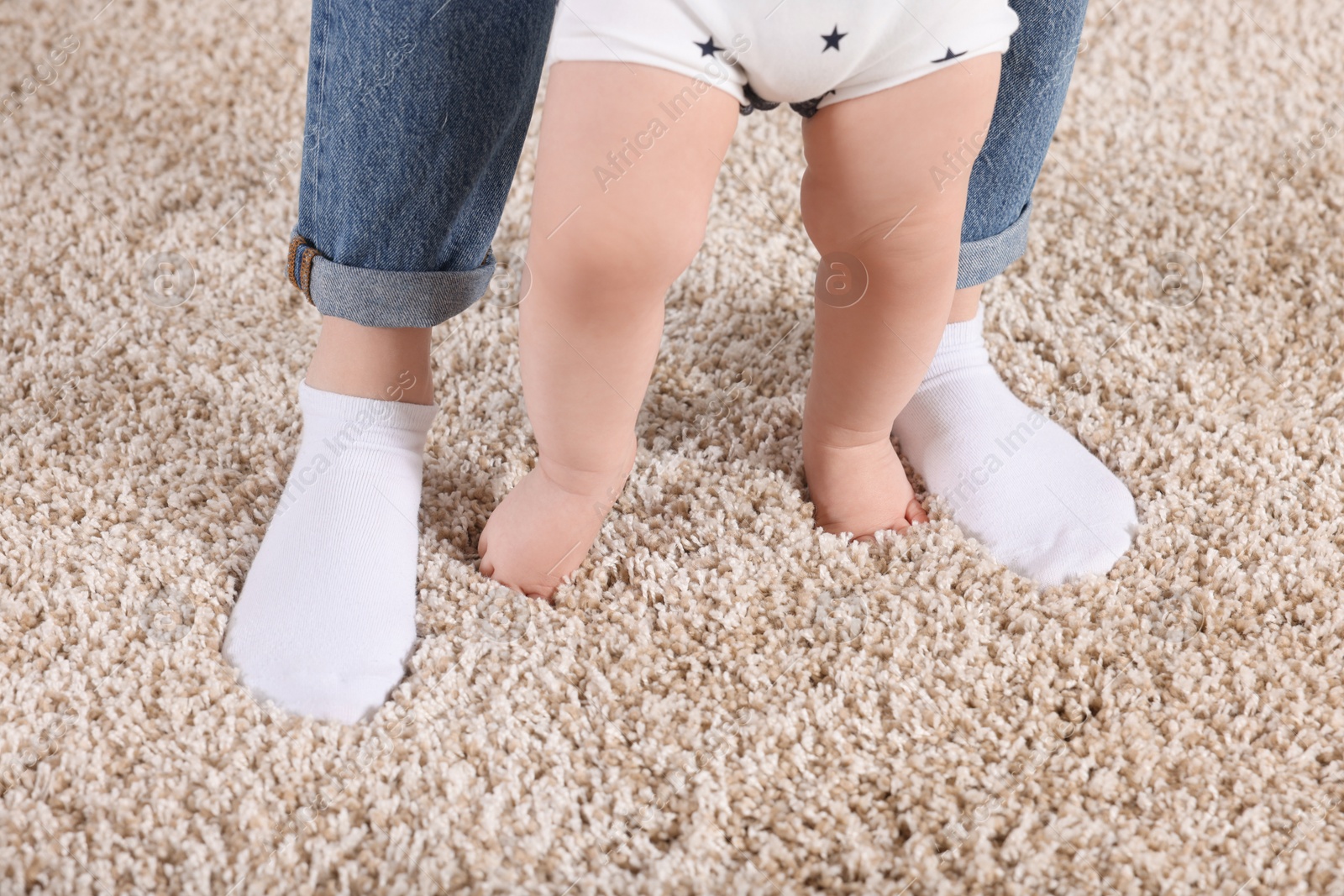 Photo of Mother supporting her baby son while he learning to walk on carpet at home, closeup