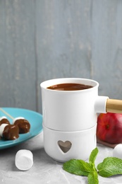 Fondue pot with milk chocolate and marshmallows on table