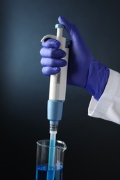 Photo of Laboratory analysis. Scientist dripping sample with micropipette into beaker on dark background, closeup