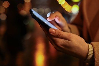 Woman using smartphone on night city street, closeup. Space for text