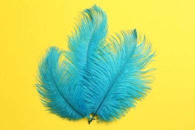 Photo of Beautiful light blue feathers on yellow background, top view