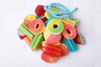 Pile of tasty colorful jelly candies on white tiled table, above view
