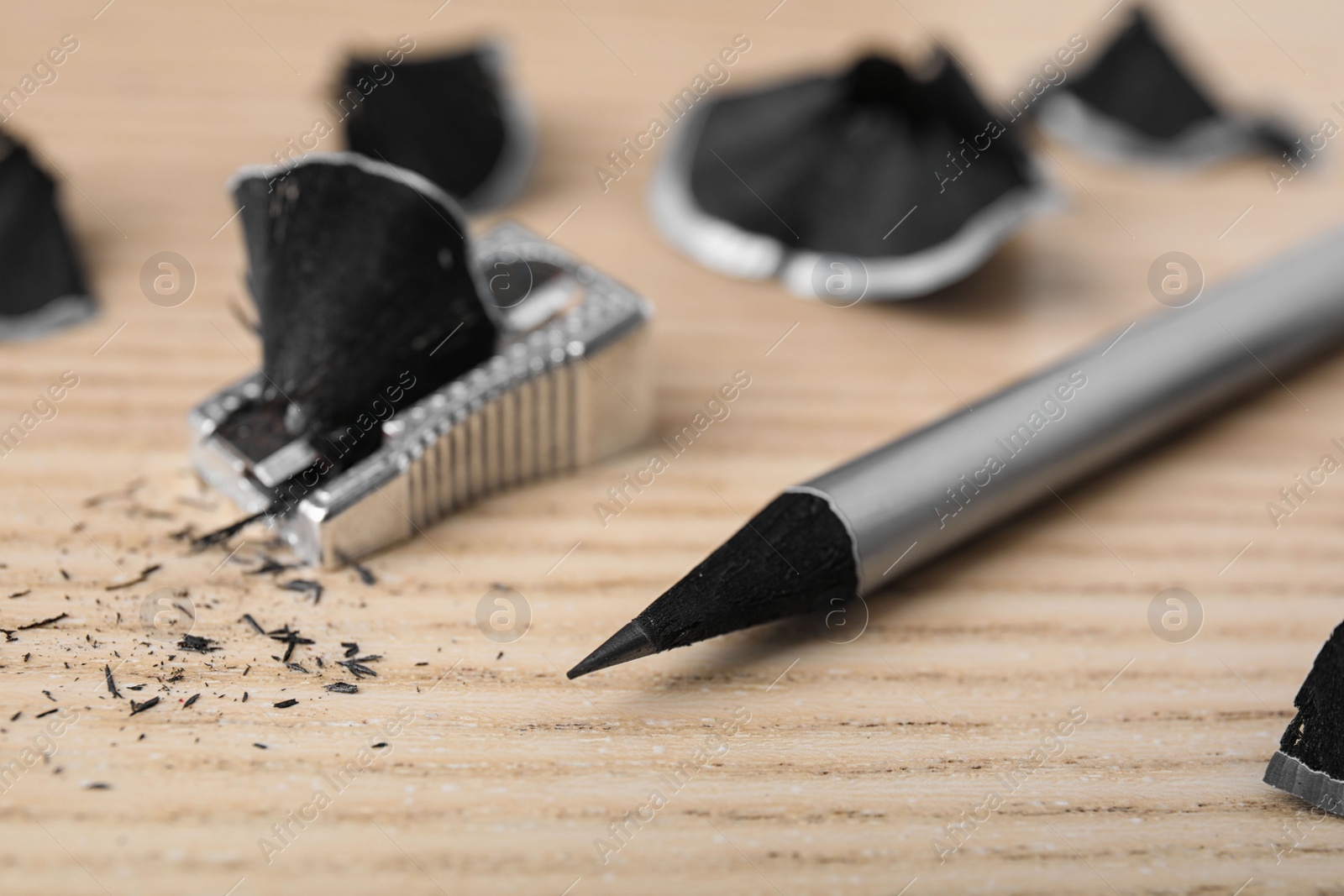 Photo of Pencil, sharpener and shavings on wooden table, closeup