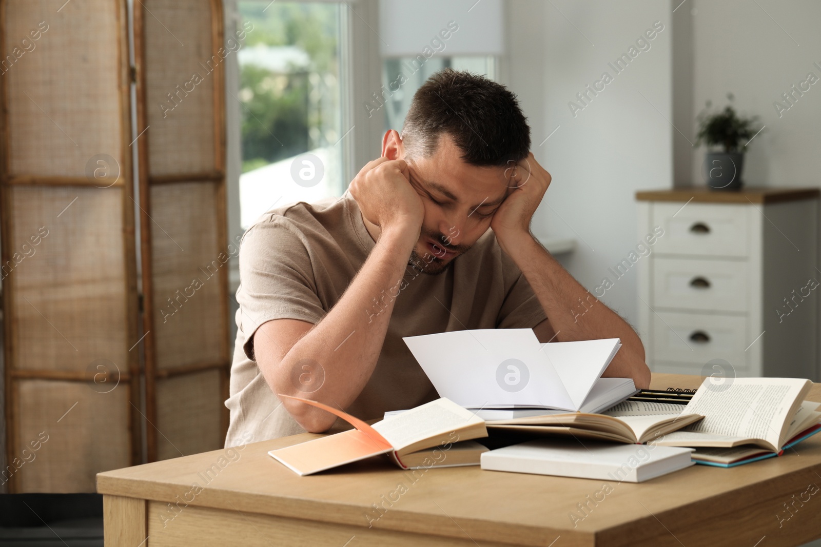 Photo of Sleepy man studying at wooden table indoors