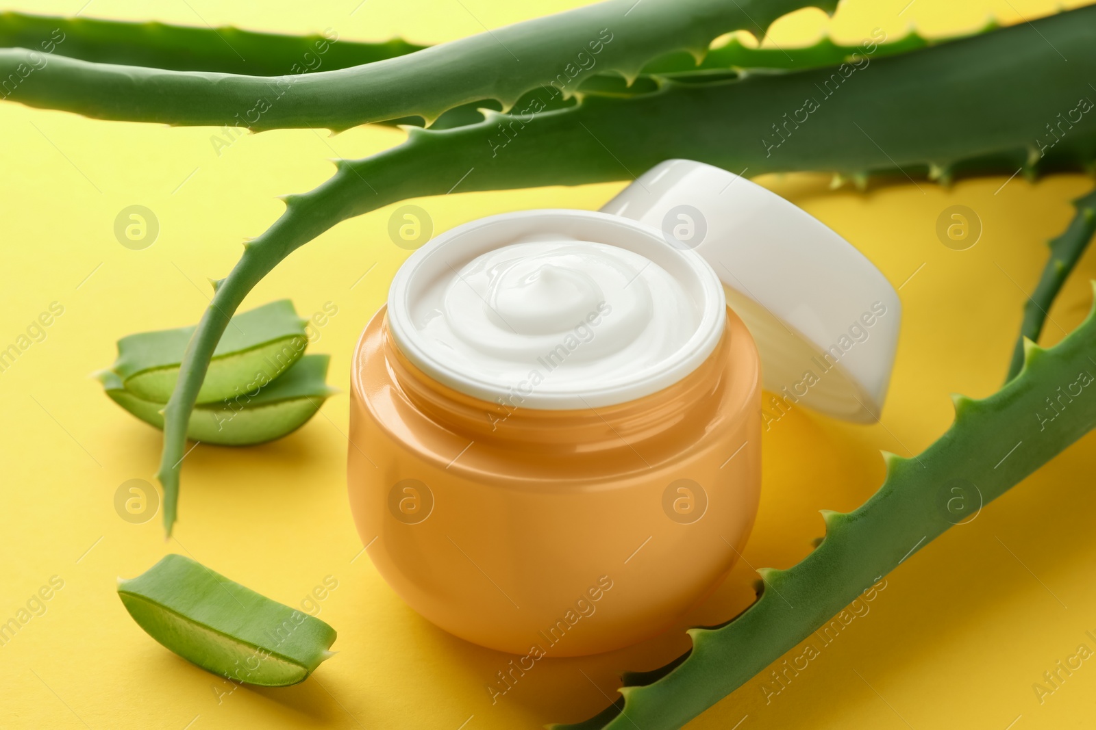 Photo of Jar with cream and cut aloe leaves on yellow background, closeup