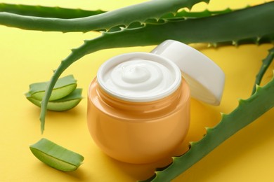 Jar with cream and cut aloe leaves on yellow background, closeup