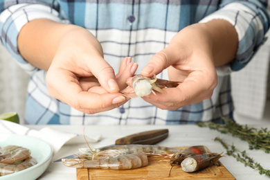 Photo of Woman peeling fresh shrimp at table, closeup