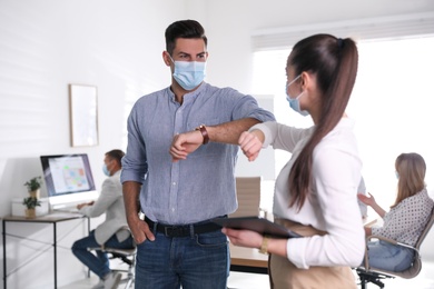 Coworkers with protective masks making elbow bump in office. Informal greeting during COVID-19 pandemic