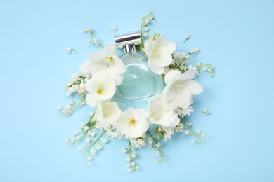 Photo of Luxury perfume and floral decor on light blue background, flat lay