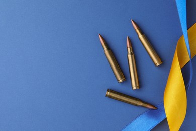 Photo of Ribbons in colors of national Ukrainian flag and bullets on blue background, flat lay. Space for text