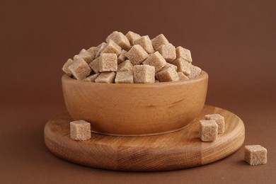 Photo of Brown sugar cubes in bowl on color background, closeup