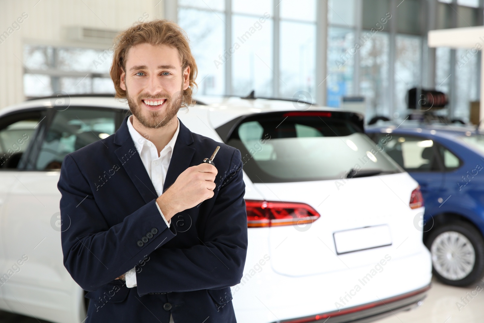 Photo of Young car salesman with key in dealership. Space for text