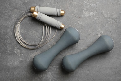 Photo of Jump rope and dumbbells on grey background, top view