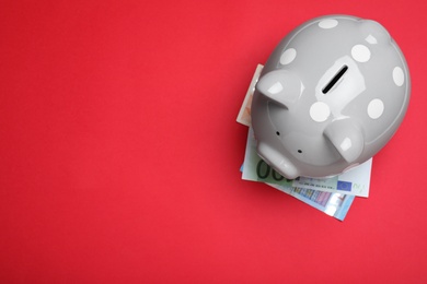 Top view of piggy bank and Euro banknotes on red background, space for text. Money savings