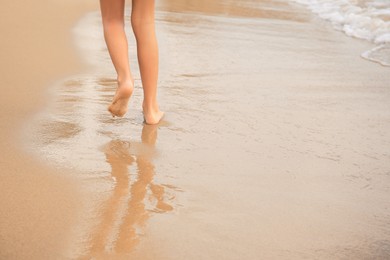 Photo of Little girl walking on sandy beach near sea, closeup. Space for text