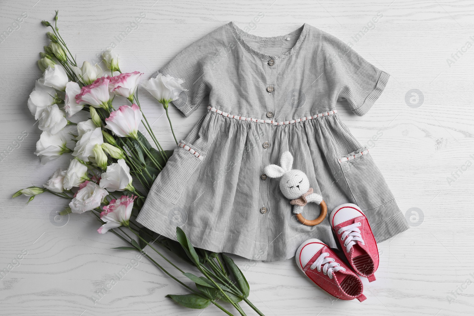 Photo of Baby dress, shoes, toy and flowers on white wooden table, flat lay