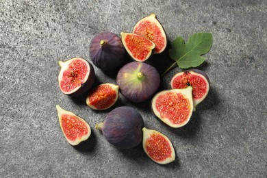 Photo of Whole and cut ripe figs with leaf on grey textured table, flat lay