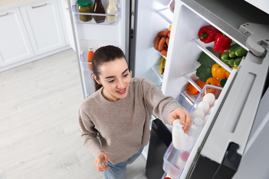 Photo of Young woman taking yoghurt out if refrigerator indoors, above view