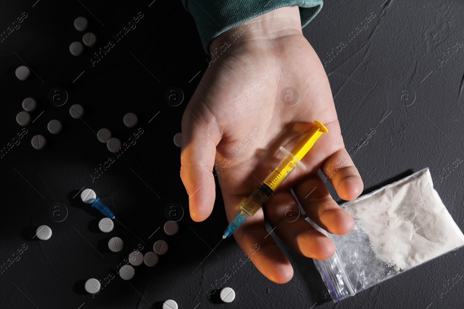 Photo of Addicted man with syringe near drugs at black textured table, top view