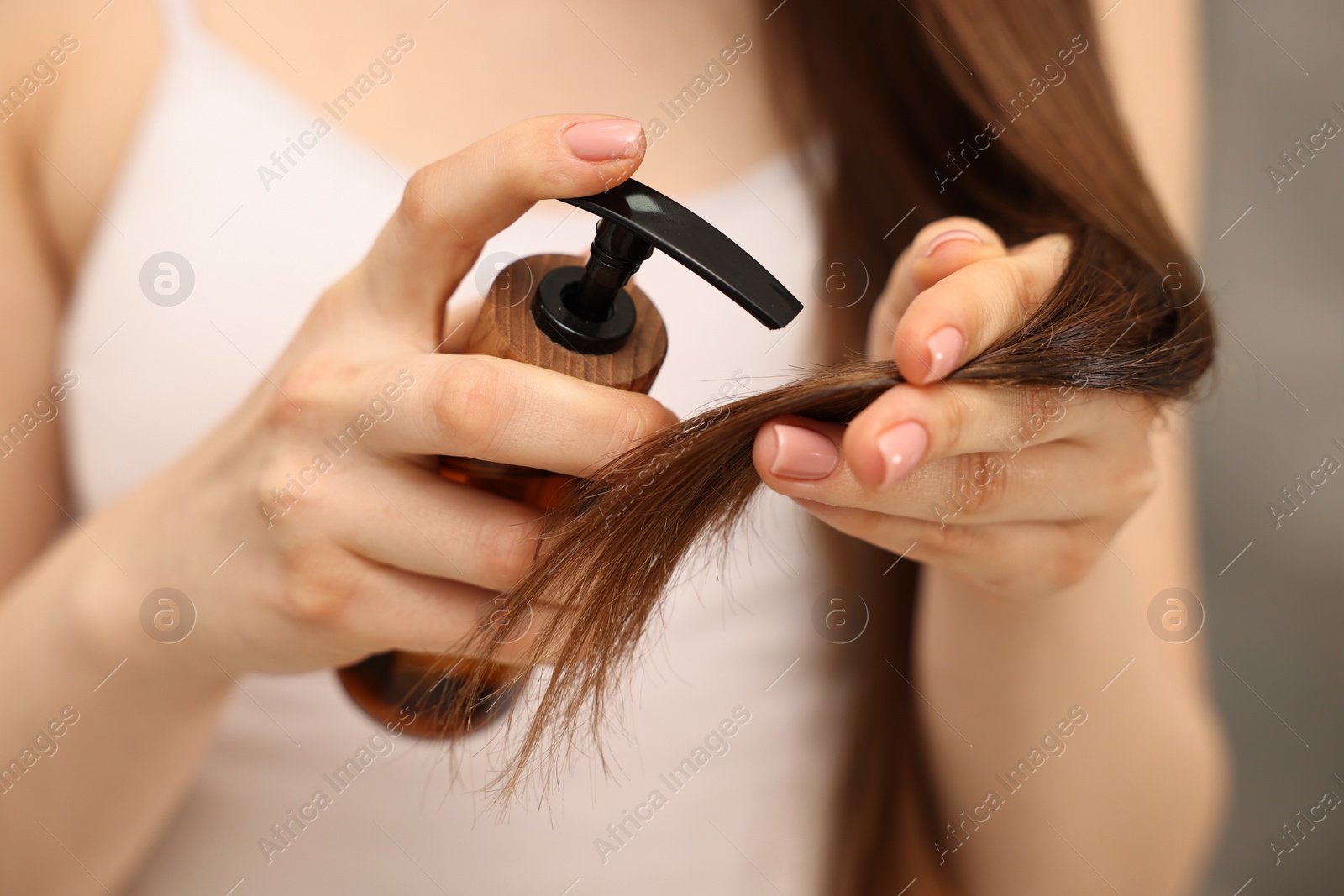 Photo of Woman applying oil hair mask indoors, closeup