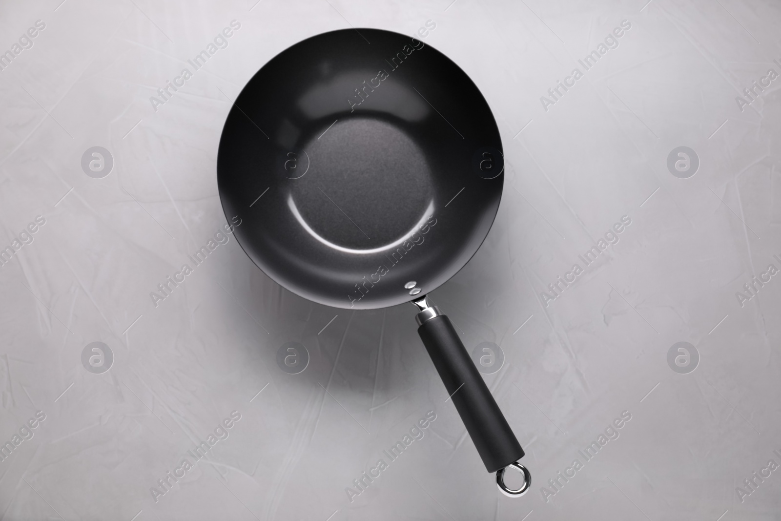 Photo of Empty iron wok on grey textured table, top view. Chinese cookware