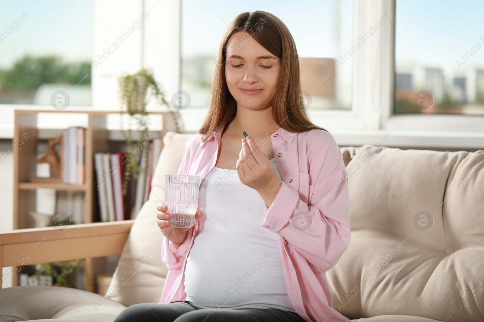 Photo of Beautiful pregnant woman holding pill and glass of water at home