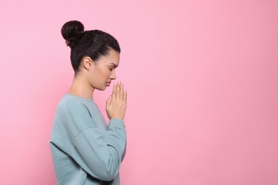 Photo of African American woman with clasped hands praying to God on pink background. Space for text