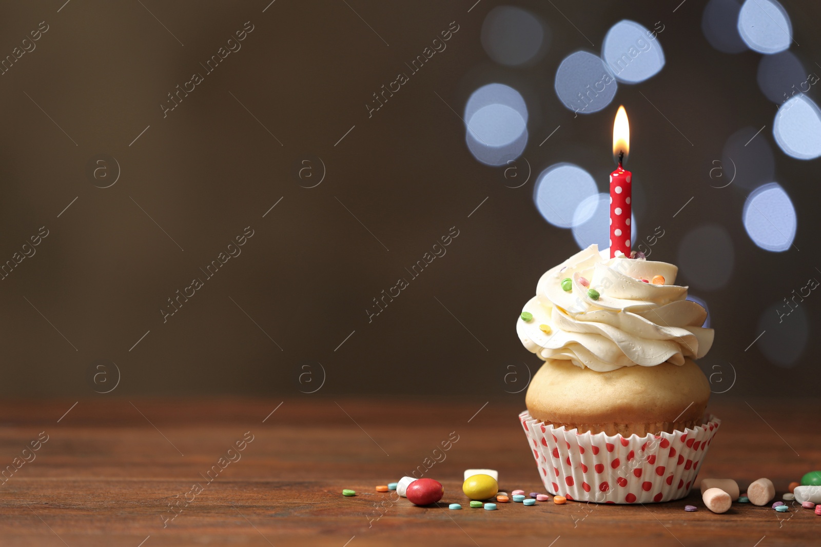 Photo of Birthday cupcake with candle on wooden table against blurred lights. Space for text