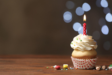 Photo of Birthday cupcake with candle on wooden table against blurred lights. Space for text