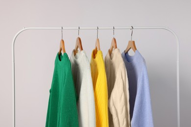 Rack with different warm sweaters on light background