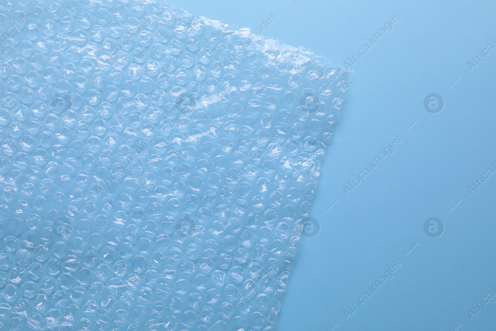 Photo of Transparent bubble wrap on light blue background, top view. Space for text