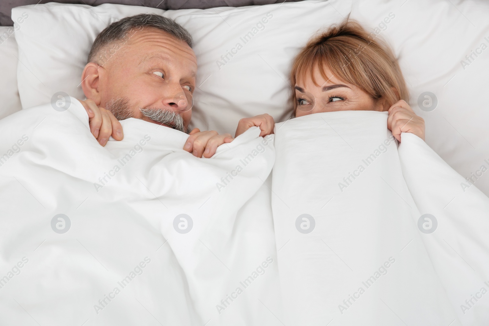 Photo of Mature couple hiding together under blanket in bed at home