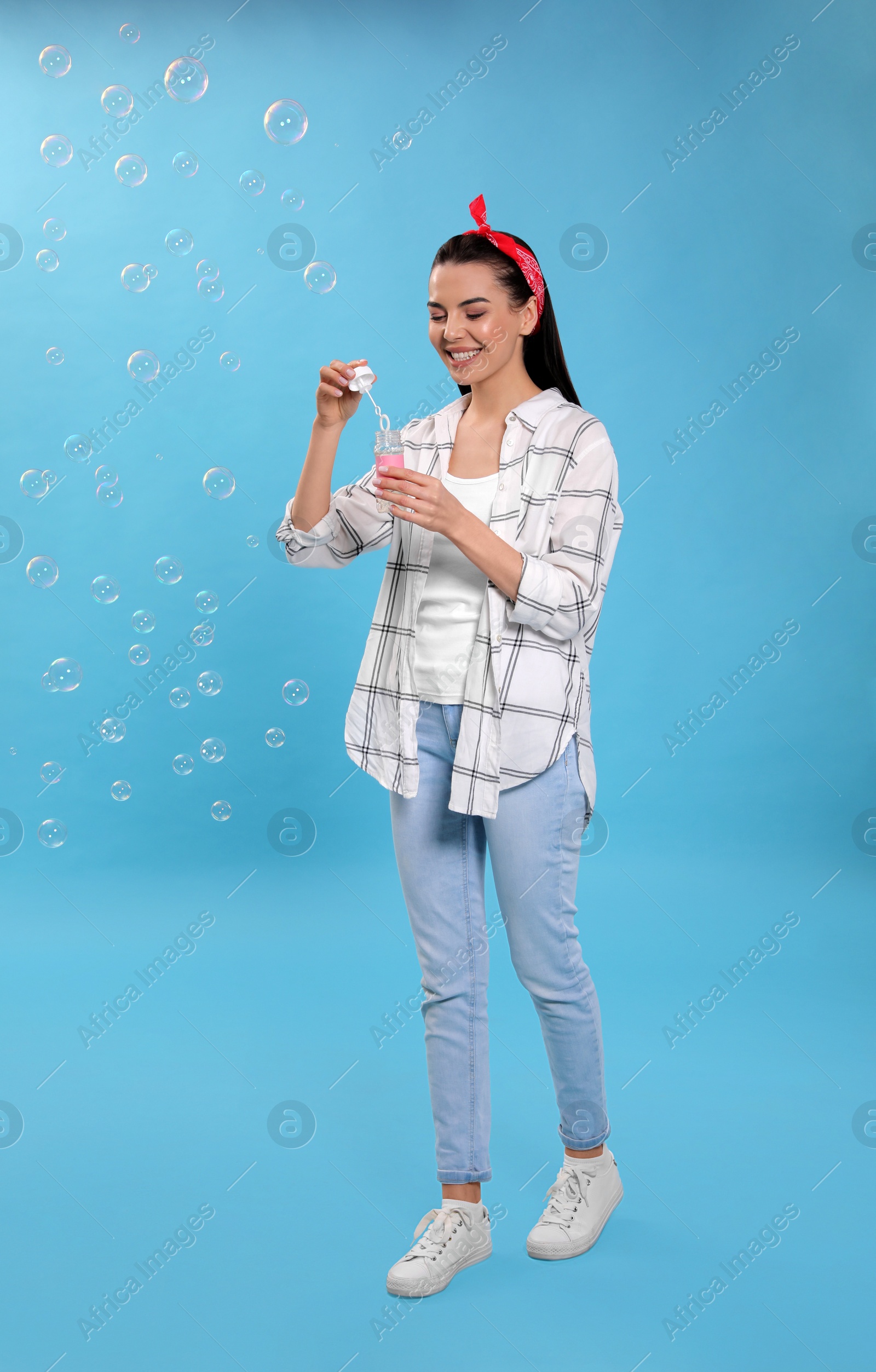 Photo of Young woman blowing soap bubbles on light blue background